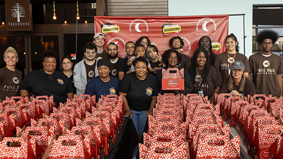 Full Sail volunteers and members of the Agape Roots Foundation pose with dozens of "Thrive Pack" care packages.