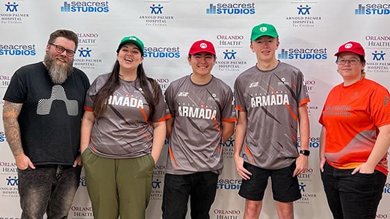 Five people posing in front of a “Seacrest Studios” backdrop, wearing Armada jerseys and hats, smiling at the camera.