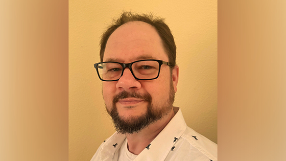 A shoulder-length photo of Sean wearing black-rimmed glasses and a white shirt.