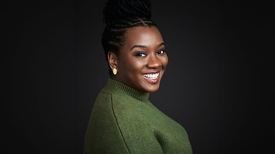 CeCe Taylor smiles at the camera. Her hair is up in a braided bun and she’s wearing a green sweater and gold earrings.