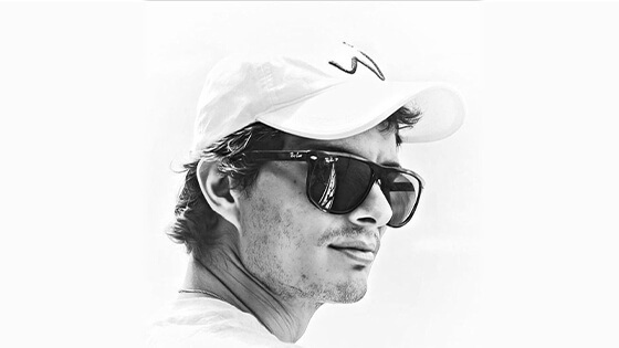 A black and white photo of Matias from the neck up, wearing a pair of sunglasses with dark frames while looking into the distance.