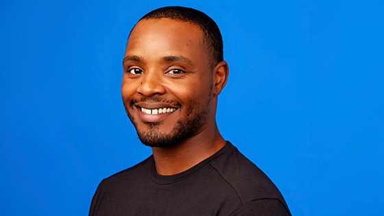 Lamont Johnson smiles at the camera in front of a blue background. He is wearing a black shirt.