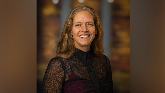 Phoebe Elefante, a woman with shoulder-length light brown hair and a black blouse smiling in front of an out-of-focus brown backdrop.