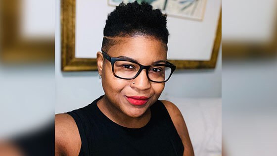 Instructor Ryan Phillips, a woman with black framed glasses and short black hair wearing a black blouse and red lipstick.