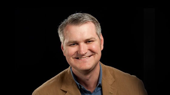 Eric Rosenfeld smiles at the camera. He has gray hair and is wearing a blue collared shirt with a tan blazer.