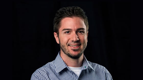 Matt is sitting in front of a black background wearing a blue plaid shirt. He is smiling.