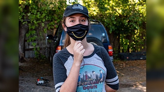 Paola Beck Gisler stands wearing a black mask with a yellow smile.