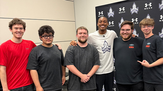 A group of five students, staff, and grads pose for a photo with NFL wide receiver Justin Jefferson in front of a step and repeat.