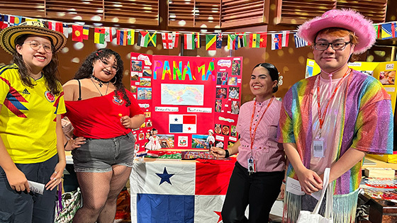 A group of smiling students stand in front of a colorful exhibit about Panama.