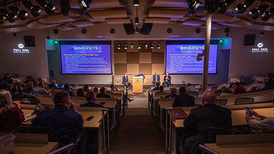 An audience watches a group of panelists give a presentation on stage at Central Florida's Second Annual Immersive Technology Summit.