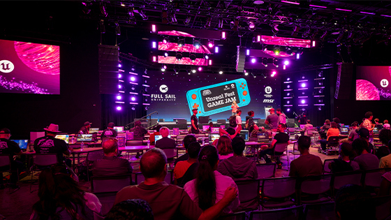 Full Sail Live, lit in a purple hue, is filled with a crowd seated at workstations during the Unreal Fest Game Jam.