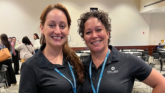 Michelle Moreno and Stacie Aldrich smiling and standing side by side wearing blue lanyards with conference badges and black Full Sail polo shirts.