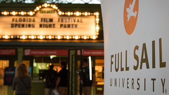 A Full Sail University banner is in focus in the foreground while the Enzian's lit-up marquee for the Florida Film Festival Opening Night Party appears in the background.