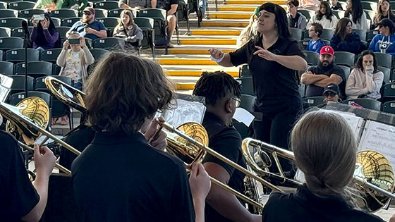 Students perform in a brass ensemble as a conductor leads, while audience members are seated in an amphitheater with Full Sail University tents in the background.