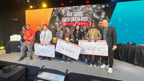 Techfest tournament winners holding large scholarship checks on stage alongside Full Sail staff members in the Fortress.