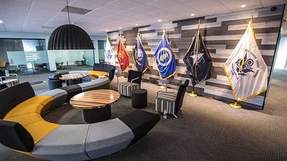 An image of Full Sail’s Military Student Success center shows a large couch, small meeting rooms, and flags representing each branch of the US Armed Services.