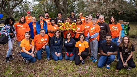 A group photo of students and staff wearing bright orange Full Sail University t-shirts. They are also holding golden balloons that spell 200.