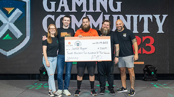 Sam Lupo, DrLupo, Bennett Newsome, and Kevin Murray on stage in the Fortress with a student in an orange Armada jersey receiving an oversized scholarship check.