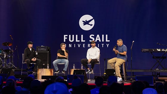 MLB Pitcher Adam Wainwright and three other people are seated on a stage during a panel, the large-scale LED screen behind them reads “Full Sail University” against a blue backdrop.