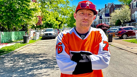 Full Sail Film Production MFA grad Panda Lord in an orange hockey jersey on a residential Philadelphia street.