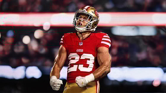 A football player in a red San Francisco 49ers jersey, number 23, celebrating passionately on the field with clenched fists.