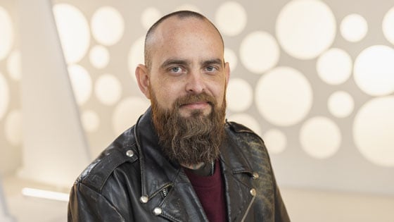 Full Sail Hall of Fame inductee Ben Rice smiles at the camera. He is wearing a burgundy sweater and a black leather jacket.