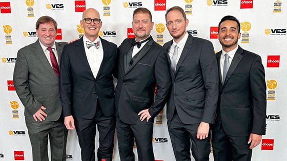 Culley Bunker stands with four special effects artists from Skulley FX in front of a VES Awards backdrop. They are wearing suits and smiling.