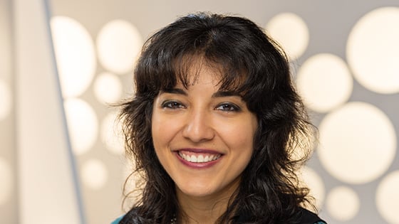 A headshot of a woman with a dark brown shag haircut smiling against a white background.