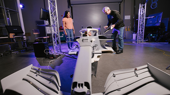 Students and an instructor work with a full-scale race car simulator model inside Full Sail’s Simulation Lab.