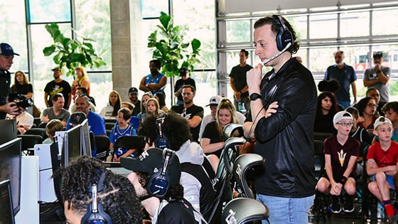 Magic Gaming’s coach and players at gaming stations while a crowd looks on in the background.