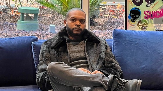 Terique Walker sits on a blue sofa wearing a black fur coat and turtleneck.