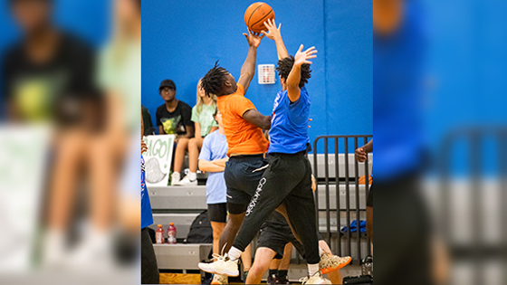 Two basketball players jump up simultaneously to reach the basketball on a court. They are both wearing athletic clothing.