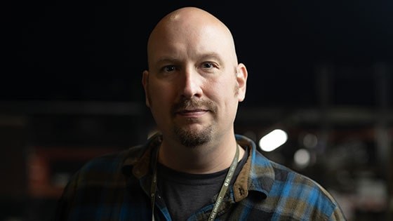 Headshot of Andrew Garraway wearing a blue and grey plaid flannel and a Full Sail lanyard, complete with Full Sail pins.