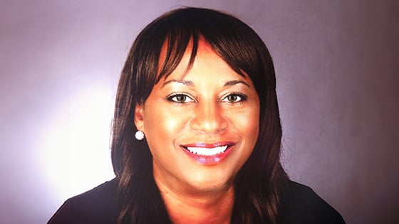 Lorraine smiles at the camera. She has dark brown hair and hazel eyes and is wearing a blue blazer and silver earrings.