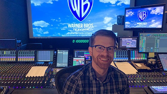 Recording Arts grad Ryan Kennedy sits in front of a large recording console.