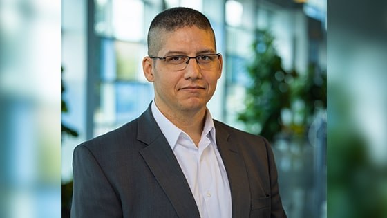 Mark Filter wears glasses, a gray suit, and a white button-down shirt. He is in one of Full Sail’s lobbies.