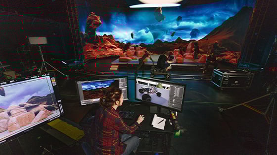 A production crew films on a sci-fi virtual set while a technician controls digital environments on monitors.