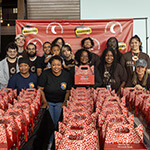 Full Sail volunteers and members of the Agape Roots Foundation pose with dozens of "Thrive Pack" care packages.
