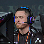 A focused esports player wearing a headset competes at a gaming event, seated between two monitors with a dark, intense atmosphere.