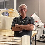 Course Director Pat Starace, a man with white hair and a grey polo shirt, standing next to a large workbench with a 3D-printed replica of a Formula 1 race car in Full Sail’s SimLab.