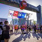 Three 5K winners stand on a podium with medals around their necks under the Full Sail Studios archway. Other competitors stand near them and applaud.