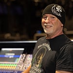 Gregg in a sound studio wearing a black beanie and graphic t-shirt. He is smiling.