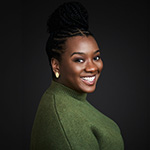 CeCe Taylor smiles at the camera. Her hair is up in a braided bun and she’s wearing a green sweater and gold earrings.