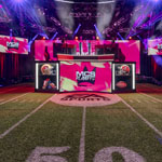 A vibrant esports stage with a football-themed setup, featuring "MCS Playoffs" branding, LED screens, and dynamic lighting.