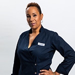 Grad Elle Simone Scott standing and smiling against a white backdrop while wearing a blue double-breasted chef's jacket with an America's Test Kitchen patch on the breast.