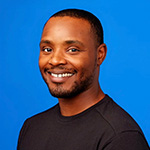 Lamont Johnson smiles at the camera in front of a blue background. He is wearing a black shirt.