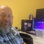 Dan Walker sits in his home office. He has a beard and is wearing a plaid shirt. A desk with several desktop monitors is behind him.
