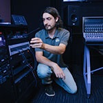 Dave Harris crouches next to broadcast equipment, including mixing consoles and a communications system.