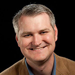 Eric Rosenfeld smiles at the camera. He has gray hair and is wearing a blue collared shirt with a tan blazer.