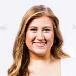 A woman smiles while holding a Full Sail 5 year anniversary guitar pick in front of a Full Sail University step-and-repeat backdrop.